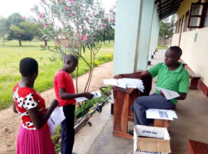 A teacher sits outside at Liberty Community High School in rural Eastern Uganda distribute learning materials to the students who are learning from home due to COVID-19